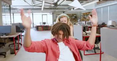 Çeşitli iş arkadaşları ofis sandalyesini masalar ve bilgisayarlar arasında gezdirirken gülüyorlar. Kutlama, takım çalışması, işbirliği, kahkaha, ofis, eğlence, çalışma alanı