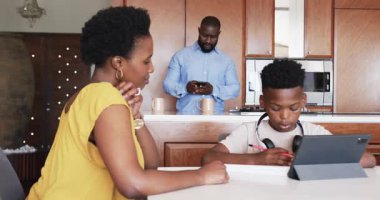 Anne ve oğlu evde tablet kullanırken baba yakınlardaki akıllı telefonu kontrol ediyor. Aile, ebeveynlik, teknoloji, aygıt, etkileşim, yerli