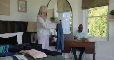 Çeşitli üst düzey çiftler seyahat planları için bavullarını, giysilerini ve danışmanlık tabletlerini hazırlıyorlar. Yaşam tarzı, organizasyon, minimalist, yerli, işbirliği, planlama, modern