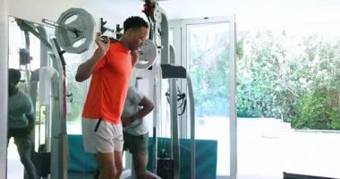 Afrika kökenli Amerikalı bir adam spor salonunda ağırlık kaldırıyor. Güç antrenmanına odaklanıyor. Spor, egzersiz, vücut geliştirme, ev çalışması, kas, halterler.