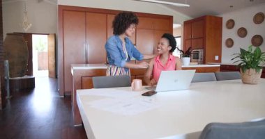 Çeşitli kadın çiftler evde başarıyı laptop ve belgelerle kutluyorlar. Kutlama, başarı, iş, ev ofisi, güçlendirme, teknoloji