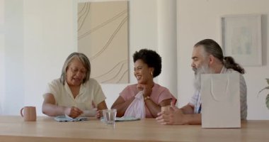 Çok nesilli aile hediye paketi açıyor. Ahşap masada pembe ve mavi giysileri ayırıyor. Aile, kaynaşma, kutlama, jenerasyon, eğlence, yerli, neşe