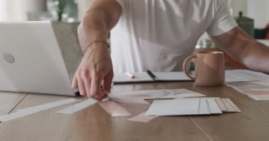 Erkek eve girer, belgeleri ahşap masaya yayar, inceler ve notlar yazar, sonra da kupayı yudumlar. Üretkenlik, ev ofisi, çalışma alanı, odaklanma, organizasyon, farkındalık, modern