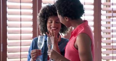 Çeşitli kadın çiftler evde şampanya bardakları tutarken muhabbet ve kahkaha atıyorlar. Kutlama, dostluk, yaşam tarzı, parti, eğlence, ev içinde