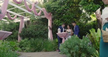 İmza defteri, pergola altında yürüyen bir çift, taç yaprakları ve baloncuklar atan misafirler, birlikteliği kutluyorlar. Aşk, kutlama, zarafet, açık hava, çiçek, mutluluk, neşe