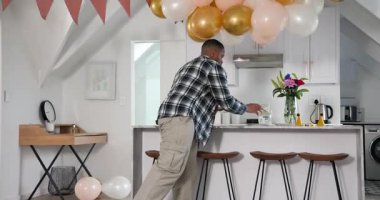 Afro-Amerikalı bir adam şarap kadehleri ve tabaklar getiriyor, balonları evde hazırlıyor. Kutlama, dekor, atmosfer, şık, uyumlu, sofistike, toplanma