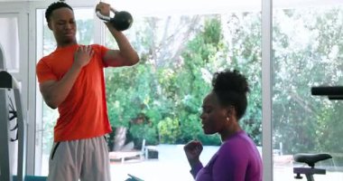 Evde birlikte egzersiz yapan genç bir çift, kollarını uzatan bir adam, izleyen bir kadın, evde spor salonu. Spor, egzersiz, ilişki, refah, sağlıklı yaşam tarzı.