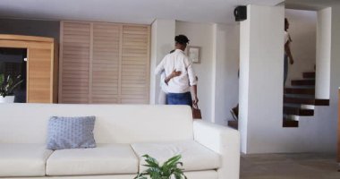 Afro-Amerikalı kadın modern oturma odasına giriyor, gülümsüyor ve rahatlamış görünüyor. Çağdaş, yaşam tarzı, rahatlama, ev, iç tasarım, mutluluk