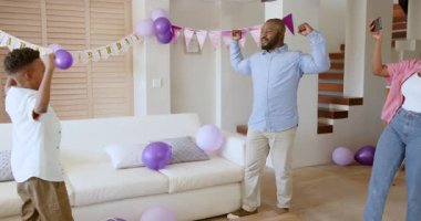 Anne anı yakalarken baba ve oğul evde neşeyle dans ediyor. Aile, bağ, samimiyet, anılar, ebeveynlik, yaşam tarzı