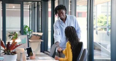 Afro-Amerikalı adam kutuyla ofise giriyor, el sıkışıyor ve eşyaları açıyor, masayı kişiselleştiriyor. İşbirliği, takım çalışması, çalışma alanı, modern, profesyonel, enerjik, üretkenlik