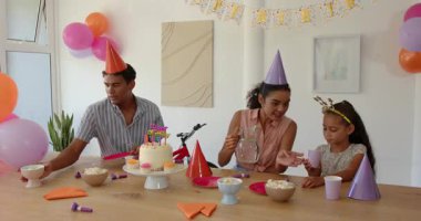 Çeşitli aileler evdeki ahşap masada oturuyor, doğum günü pastasının ve bayramlık ikramın tadını çıkarıyorlar. Kutlama, aile, atıştırmalıklar, doğum günü, parti, eğlence, birliktelik, dekorasyon