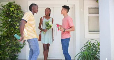 Ev sahibi, farklı arkadaşlar buket ve hediye kutusu sunarken sürgülü kapıyı açıyor. Kutlama, misafirperverlik, dostluk, modern, misafirperver, açık hava, neşeli