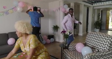 Cinsiyet belirleme partisinde evde bebek ayakkabısı tutan adam şaşırmış görünüyor. Ebeveynlik, kutlama, aile, beklenti, gelenek, mutluluk