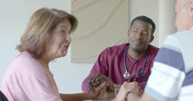 Afro-Amerikan tedarikçi ahşap masaya gelip yaşlı çifti selamlıyor ve su bardağını işaret ediyor. Şefkat, iletişim, empati, sağlık, profesyonellik, sıcak, güven