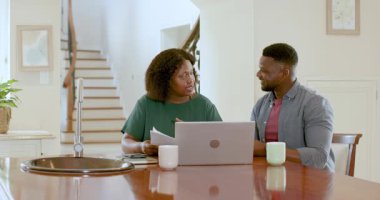 Olgun çift mutfak masasında dizüstü bilgisayar kullanırken belgeleri tartışıyor. Buluşma, planlama, danışma, teknoloji, yaşam tarzı, ortaklık