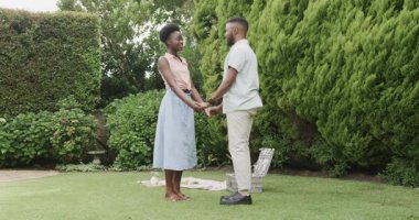 Genç bir adam bahçede, yemyeşil çimlerle çevrili bir kadına sürpriz yapmayı teklif ediyor. Romantizm, evlilik teklifi, nişan, aşk, çift, açık hava