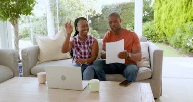 Afro-Amerikalı çift evdeki kanepede oturuyor, gülümsüyor ve sarılıyorlar. Aile, aşk, birliktelik, sevgi, mutluluk, arkadaşlık.