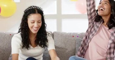 İki bayan arkadaş konfeti kepçeliyor ve kanepeye konfeti üflüyor doğum günü kutlaması için. Kutlama, dostluk, neşe, şenlik, atmosfer, mutluluk, coşku