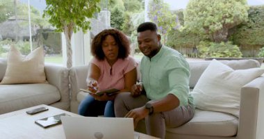 Evde dizüstü bilgisayar ve defter kullanarak plan yapan Afro-Amerikan çift. Takım çalışması, işbirliği, teknoloji, yaşam tarzı, dijital, samimi