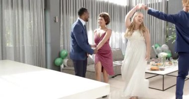 Mutlu gelin, damat ve arkadaşları oturma odasında bir düğün resepsiyonunda dans ediyorlar. Kutlama, düğün, ilişki, parti ve arkadaşlık kavramı.