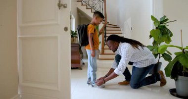 Mutlu siyah baba konuşuyor ve çok ırklı oğlunun ayakkabı bağcıklarını topluyor. Okula gitmeden önce evdeki koridorda. Eğitim, okul, aile, çocukluk, ev hayatı ve ilişki kavramı.