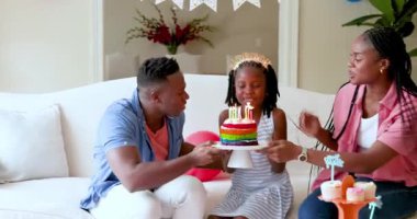 Mutlu siyah çift ve kızları doğum gününü kutluyor, kız evde doğum günü pastasından mum üflüyor. Doğum günü, kutlama, parti, aile, çocukluk, ev hayatı ve ilişki kavramı.