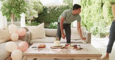 Genç çift oturma odasında pasta ve balonlarla doğum günü kutlaması hazırlıyor. Parti, neşe, dekorasyon, şenlik