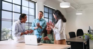 Dizüstü bilgisayarın etrafında çalışma ve ofiste kutlama konularını tartışan mutlu meslektaşlar. Takım çalışması, iş, kutlama ve iletişim konsepti.