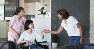 Tekerlekli sandalyede oturan mutlu son sınıf öğrencisi kadın hemşire ve bayan arkadaşıyla oturma odasında konuşuyor. üst düzey yaşam tarzı, engellilik, sağlık ve arkadaşlık konsepti.