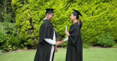 Bahçede birbirine gülümseyen kep ve cüppeli mezuniyet çifti. Mezuniyet, kutlama, başarı, akademik, diploma, açık hava