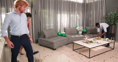 Mutlu damat ve farklı arkadaşlar oturma odasındaki düğün resepsiyonundan sonra konfeti temizliyor. Kutlama, düğün, ilişki, parti ve arkadaşlık kavramı.