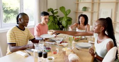 Çeşitli arkadaşlar ahşap masa partisinde yemek yiyor, yemek tabakları, içkiler ve yemyeşil manzaranın tadını çıkarıyor. Toplama, mutfak, atmosfer, sosyalleşme, rahatlama, güneş ışığı, arkadaşlık