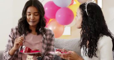 Çok ırklı anne ve genç kız, balonların yanındaki koltukta mor bardaklarını yudumluyorlar. Aile, kaynaşma, birliktelik, parti, rahat, rahat, pastel