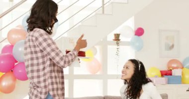 Oturma odasındaki gri koltukta oturan çeşitli bayan arkadaşlar doğum gününü pastayla kutluyorlar. Parti, toplanma, şenlik, kahkaha, içecek, patlamış mısır, punç