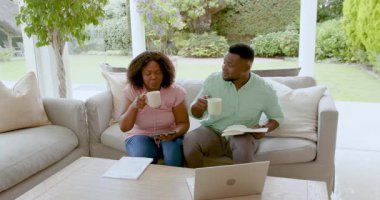 Kanepede dizüstü bilgisayar ve belgelerle birlikte finansman yapmayı planlayan Afro-Amerikalı çift. Bütçe, ev ofisi, takım çalışması, teknoloji, finans, yaşam tarzı