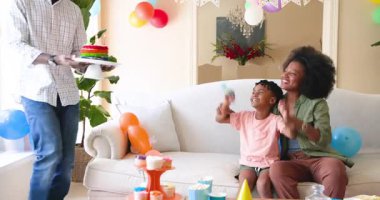 Mutlu siyahi çift ve onların çok ırklı oğlu, çocuğun doğum gününü evde kutluyor, çocuk pastaya mum üflüyor. Doğum günü, kutlama, parti, aile, çocukluk, ev hayatı ve ilişki kavramı.