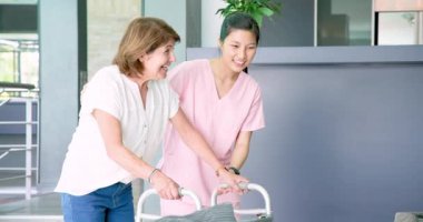 Hemşire kız arkadaşıyla oturma odasında konuşurken yürüyüş çerçevesi kullanan mutlu kıdemli kadın. üst düzey yaşam tarzı, engellilik, sağlık ve arkadaşlık konsepti.