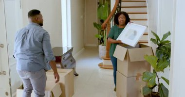 Yeni evdeki kutuları açarken duvarda sanat eserleri düzenleyen çift. Taşınma, taşıma, iç mekan, dekorasyon, yerleşim