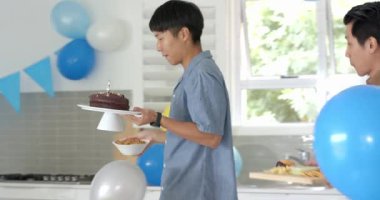 Asyalı baba ve oğul, arka planda renkli balonlarla evde sımsıkı sarılıyorlar. Arkadaşlık, kutlama, mutluluk, bağlantı, parti, neşe