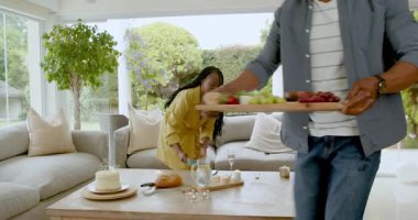 Afro-Amerikalı adam, oturma odasında pasta ve içeceklerle masayı hazırlıyor. Kutlama, misafirperverlik, parti, tatlı, içecek, toplanma