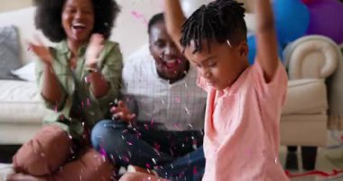 Mutlu siyah çift ve onların çok ırklı oğlu konfeti atıyor ve gülümsüyor, çocuğun doğum gününü evde kutluyorlar. Doğum günü, kutlama, parti, aile, çocukluk, ev hayatı ve ilişki kavramı.