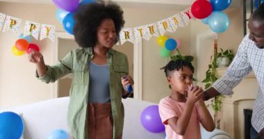 Mutlu siyah çift ve onların çok ırklı oğulları balon şişiriyorlar, evde oğlanın doğum gününü kutluyorlar. Doğum günü, kutlama, parti, aile, çocukluk, ev hayatı ve ilişki kavramı.