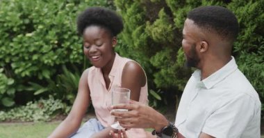 Genç çift parkta piknikten keyif alıyor, gülümsüyor ve çimenlerde birlikte dinleniyorlar. Açık hava, rahatlama, doğa, mutluluk, bağ, rahatlık.