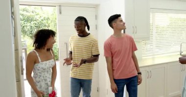 Ahşap adası ve saksı bitkisi olan parlak, ferah bir mutfakta yemek pişiren çeşitli arkadaşlar. Mutfak, doğal ışık, birliktelik, modern, arkadaşlık, yemek pişirme, gündelik