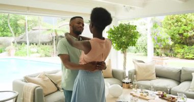 Genç çift oturma odasında birlikte dans ediyor, evde mutlu anların tadını çıkarıyorlar. Dans, mutluluk, romantizm, yaşam tarzı, kutlama, ilişki