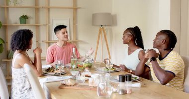 Ahşap yemek masası partisinde oturan çeşitli arkadaşlar tabaklar, şarap ve lambayla yemeğin tadını çıkarıyorlar. Yemek, arkadaşlık, mutfak, toplanma, kahkaha, dekor, sıcaklık.