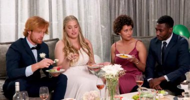 Mutlu gelin ve damat ve farklı arkadaşlar oturma odasındaki düğün resepsiyonunda yemek yiyorlar. Kutlama, düğün, ilişki, parti ve arkadaşlık kavramı.