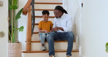 Mutlu siyah baba ve çok ırklı oğlu merdivenlerde oturmuş kitap okuyorlar, anne oğlunu kucaklıyor. Eğitim, okul, aile, çocukluk, ev hayatı ve ilişki kavramı.
