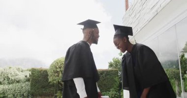 Mezuniyet elbiseleriyle, çift başarıyı dışarıda diplomalarla kutluyor, neşeyle gülümsüyor. başarı, tören, kutlama, mutluluk