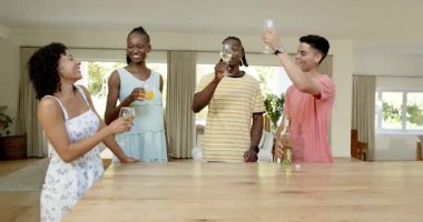 Modern mutfakta sohbet eden ve gülen farklı arkadaşlar, ahşap masada içki içiyorlar. Toplanma, atmosfer, kutlama, arkadaşlık, modern, etkileşim, rahatlama